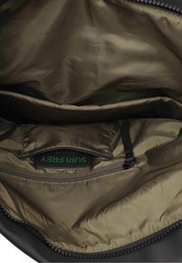 Svart väska med glansigt olivfärgat foder. Har ett dragkedjefack och en etikett med texten "SURFERY GREEN LABEL" i grön text. Mjuk textur.