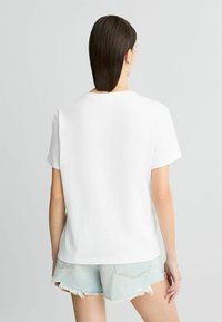 T-shirt blanc à manches courtes avec une coupe décontractée, col rond, texture lisse et ourlet droit, associé à un short en denim clair.