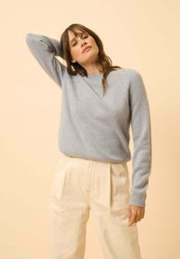 Lichtblauwe gebreide trui met een ronde halslijn, geribbelde manchetten en een relaxed fit; gecombineerd met beige geplooide broeken.