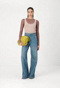 Šviesiai rožinė be rankovių palaidinė dėvima ant ilgomis rankovėmis rudos spalvos marškinėlių; šviesiai mėlynos spalvos aukštakulnės džinsinės kelnės; rankose laikomas sutrauktas geltonas šalikėlis.