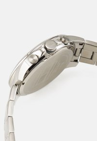 Silberner Edelstahl-Uhr mit strukturiertem Lünette, doppelten Drückern und einem polierten Gehäuse. Glatte Metallarmbandglieder unterstreichen ihr elegantes Design.