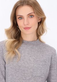 Pulover gri tricotat cu guler rotund și o mică buzunar frontal. Materialul pare moale, având o textură netedă. Variații subtile în culoarea gri.