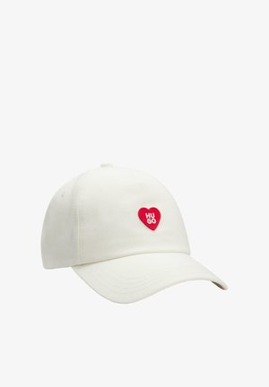 Cotton baseball cap in off-white with a curved brim and a red heart patch featuring "HUGO" text. Simple, clean design with textured fabric.