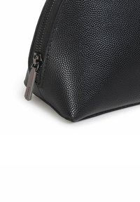 Czarna, teksturowana kosmetyczka w kształcie trójkąta, z zamkiem błyskawicznym i metalowym tagiem, wykonana z trwałego materiału syntetycznego.