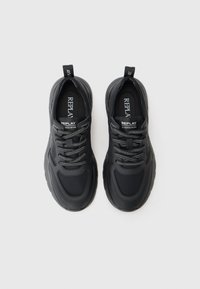 Chaussures de sport noires avec une tige texturée, un bout rond et une semelle rembourrée. Comprend des lacets réfléchissants et une languette de traction en boucle au talon.
