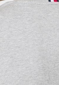Tela gris claro con una textura suave, con un escote horizontal y acentos de tela en rojo, blanco y azul marino en la parte trasera.