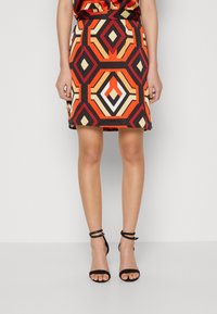 Sukně s vzorem featuring geometrický design v červené, oranžové, černé a krémové barvě. Vyrobena z hladkého materiálu s přiléhavým střihem a viditelným lemem.