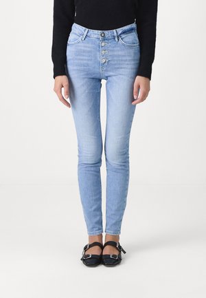 Jeans de tiro alto de color azul claro con cierre de botones, cinco bolsillos y un diseño de pierna ajustada, combinados con zapatos negros con tiras.