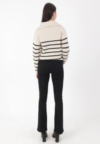 Beige gestreifter Pullover mit schwarzen Horizontalstreifen und hohem Kragen. Kombiniert mit schwarzen ausgestellten Hosen und klobigen schwarzen Stiefeln.