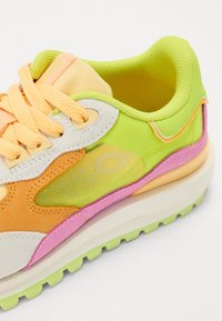 Sneaker multicolore avec une tige en mesh verte, orange et jaune, un accent rose et une semelle blanche épaisse. Lacets texturés inclus.