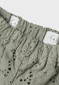 Olijfgroene, gemêleerde stof met bloemenborduursels, gegatherde taille met elastiek en witte knoopsluiting.