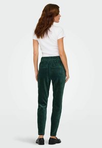 Zielone spodnie korduroy o slim fit, z elastycznym pasem i dwoma tylnymi kieszeniami. Połączone z gładką białą koszulką i czarnymi butami.