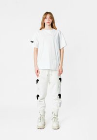 Camiseta blanca oversized con un parche rectangular. Pantalones de chándal blancos con detalles de bordado en blanco y negro. Botas color crema.