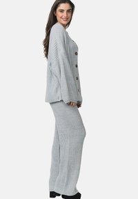 Set di abbigliamento da casa grigio chiaro in maglia, con un maglione largo caratterizzato da spacchi laterali e grandi bottoni, abbinato a pantaloni a gamba larga in maglia a coste.