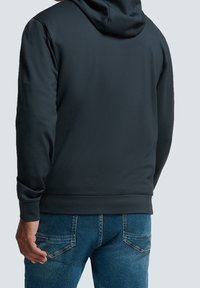 Felpa nera con cappuccio realizzata in tessuto morbido, dotata di tasca a marsupio e polsini a costine, abbinata a jeans in denim blu.