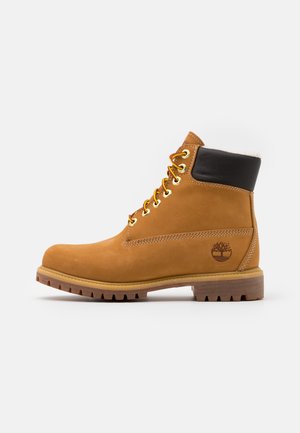 Tan leather ankle boot with black collar, gold eyelets, and laces. Textured sole with tread pattern and logo on the side.