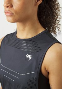 Svart trenings tank top med ergonomisk design, som har teksturerte mesh-paneler og hvit logo på brystet. Glatt stoff med kontrastlinjer.