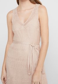 Robe en maille rose pâle avec un col en V, sans manches, motif zigzag texturé et détail de ceinture à nouer.