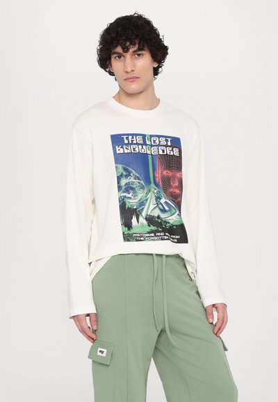White long-sleeve T-shirt featuring a graphic print in blue and green, paired with green sweatpants with side pockets and drawstring waist.