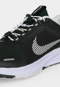 Ασπρόμαυρο παπούτσι για τρέξιμο Nike με ριγέ λογότυπο swoosh, λευκά κορδόνια με σχέδιο και λευκή σόλα, εμφανίζεται κοντινό.
