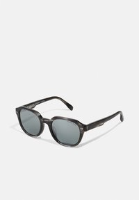 Ochelari de soare oversized negri-gri cu lentile întunecate și o ramă din plastic lucios. Prezintă accente metalice și numele mărcii gravat pe brațe.