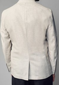 Lys beige linned blazer med en tekstureret finish, enkelt ventilationshul bagpå og diskrete skulderpuder. Har mørke knapper på ærmerne.
