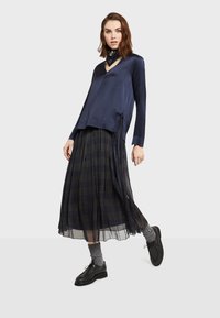 Mornarica saten košulja dugih rukava s V-izrezom i bočnim mašnama, uparen s plisiranom, prozirnom crnom kariranom suknjom i crnim čipkastim cipelama.