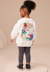 White sweatshirt with a colorful graphic featuring playful designs, paired with gray ribbed leggings and black high-top shoes.