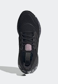 Scarpa sportiva nera con tomaia in tessuto testurizzato, lacci e suola decorata con macchie bianche e disegni floreali. Dettaglio rosa sulla linguetta.