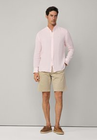 Camisa de lino rosa claro con cuello abotonado, combinada con pantalones cortos beige y mocasines marrones, con un diseño simple y un corte relajado.