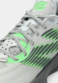 Grå og grøn atletisk sko med mønstrede snørebånd, neongrønt logo og struktureret sideskønhed vist i tæt på detalje.