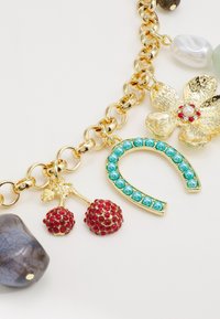 Bracelet en chaîne dorée orné de charms variés : cerises en cristal rouge, fer à cheval accentué de turquoise et fleur dorée texturée avec perle.
