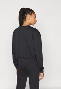 Μαύρο φούτερ με στρογγυλή λαιμόκοψη, άνετη εφαρμογή και ριμπ μανσέτες. Φορεμένο με αντίστοιχο σκούρο παντελόνι, παρουσιάζοντας ένα απλό, απλοϊκό σχέδιο.