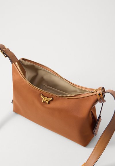 Brun crossbody-väska med guldzipper och emblem, delvis öppen som visar beige inredning och justerbar läderrem med spänne.