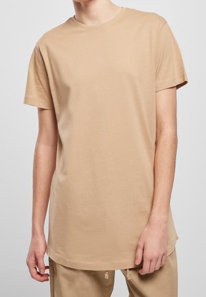 T-shirt in cotone beige con maniche corte, scollatura rotonda e orlo più lungo. Tessuto liscio con dettagli di cucitura minimi.
