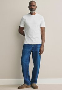 Weißes Baumwoll-T-Shirt, blaue gerade Jeans und braune Wildledersneakers. Einfaches Design, kontrastierende Farben und bequeme Passform.