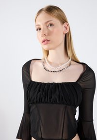 Schwarzes, durchsichtiges Langarmshirt mit gerafftem Ausschnitt und Glockenärmel. Es verfügt über geschichtete Halsketten mit abwechselnden Perlen und metallischen Akzenten.