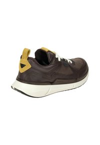 Zapatillas de cuero marrón con suela blanca, acentos amarillos, paneles texturizados y una tira en el talón. Los cordones son blancos.