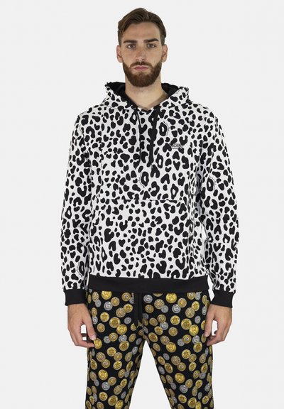 Felpa con stampa leopardata bianca e nera, dotata di tasca frontale e polsini neri. Abbinata a pantaloni neri decorati con motivi di monete dorate e argentate.