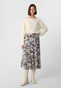 Crème trui met lange mouwen, gecombineerd met een grijze, gemusterde gelaagde rok met bloemenontwerpen. Beige kniehoge laarzen maken de outfit compleet.