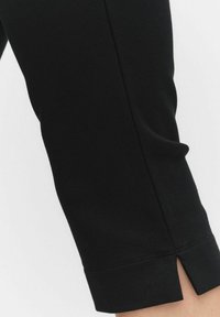 Svarta stretchiga byxor med smal passform, som har en spalt detaljerad nederkant och synliga sömmar för ökad struktur.