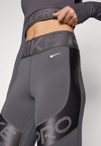 Gray athletic leggings with a wide branded waistband, featuring a sleek design, stretch fabric, and black accents for added detail.