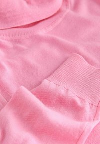 Pink cotton fabric displayed, with a soft texture. The fabric features a smooth finish and ribbed cuffs, showcasing gentle folds and creases.
