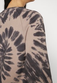 Beige sweatshirt med svart tie-dye mönster. Har en rund halsringning och strukturerad tyg, som visar ett spiral-liknande mönster över axeln.