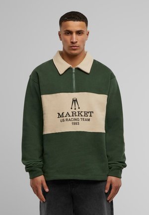 Grüner und beiger Pullover mit Reißverschlusskragen, der einen Front-Logo-Druck mit der Aufschrift "MARKET US RACING TEAM 1993" aufweist. Weiche Textur.