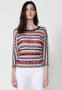 Pulover tricotat cu un model colorat în dungi roșii, verzi, albastre și crem. Mâneci trei sferturi și decolteu rotund. Textură de plasă.
