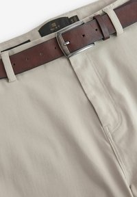 Pantalones de algodón beige con un cinturón de cuero marrón y hebilla de metal plateado, cinturilla con costuras cuidadas y detalles en los bolsillos laterales.