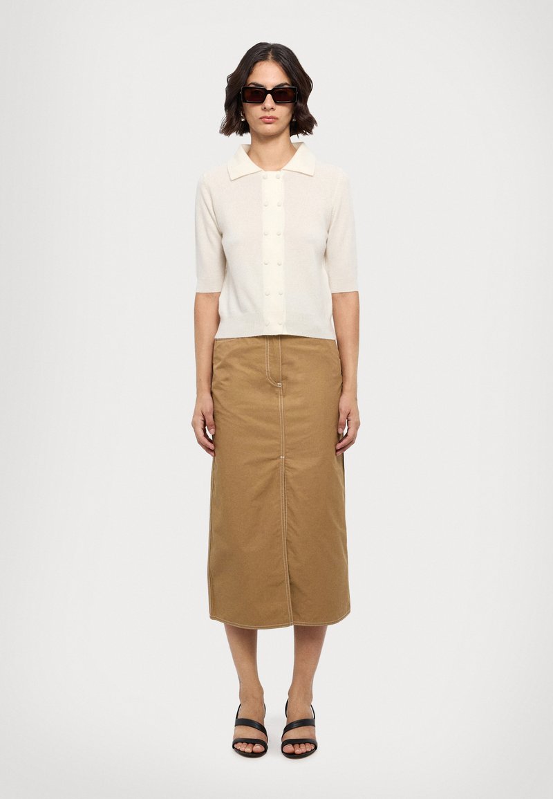 Top de punto de manga corta en beige claro con cuello y una tapeta de botones en la parte delantera, combinado con una falda caqui hasta la rodilla que presenta una costura central.