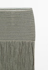 Vævet tekstil med vandrette sorte striber på en lys baggrund, med frynseudsmykninger i bunden, der skaber et tekstureret udseende.