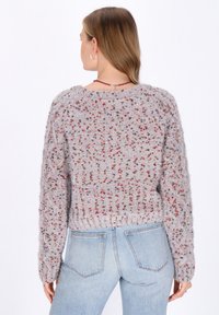 Pulover gri tricotat cu o suprafață texturată, având stropi multicolori. Design scurt și tiv zimțat. Asortat cu blugi de un albastru deschis.
